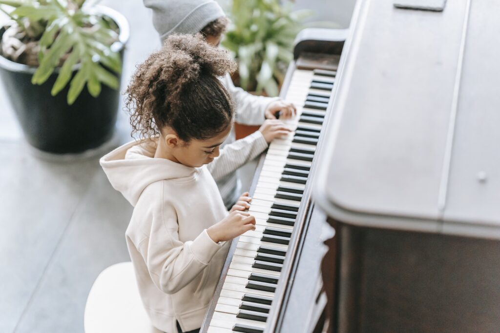 High angle side view of anonymous ethnic children in casual clothes playing piano together at home near potted plants with green leaves